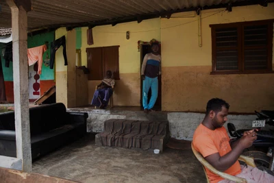 Sreerangan (the elderly one) and his late wife Maheswari came from Ceylon, present day Sri Lanka, to Tamil Nādu, post-independence of India. He says their daughter Parvathi was borne in Tamil Nādu, years before the family migrated to Kodimbala village in Dakshin Kannada district, Karnataka, in search of work in a government owned rubber estate. Sreerangan's grand childred were born in Karnataka. They are also working at the rubber estate. The younger one Chetan is playing a game in the mobile phone, Soorya is standing at the door.