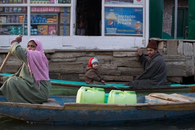 On an outing with children, they stopped at a floating shop in Dal lake. A small beautiful girl is just shadowed by a generous woman passing with drinking water.
